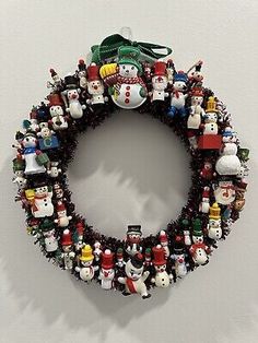 a christmas wreath made out of many different types of ornaments on a white wall with a green ribbon