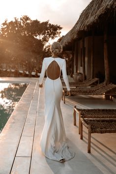 a woman in a long white dress is walking towards the pool with her back to the camera