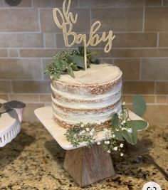 a cake with greenery on top sitting on a counter next to a wooden sign that says oh baby