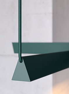 a green metal object hanging from a wire next to a white brick wall with a light on it