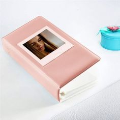 a pink photo album sitting on top of a white table next to a blue box