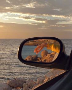 a side view mirror with a hand sticking out of it's reflection next to the ocean