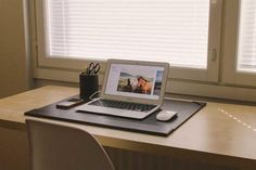 an open laptop computer sitting on top of a wooden desk next to a white chair