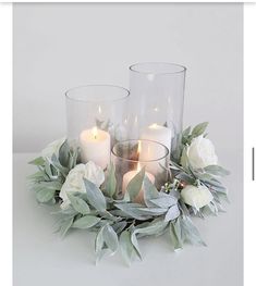 some candles are sitting on a table with flowers and greenery around the candle holders