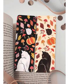 two notebooks sitting on top of an open book with autumn leaves and cats printed on them