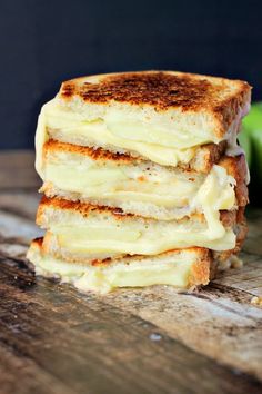 four grilled cheese sandwiches stacked on top of each other with apples in the background