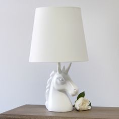 a white horse head lamp sitting on top of a wooden table next to a flower