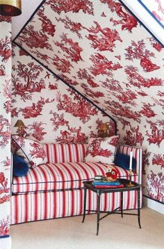 a red and white bed sitting under a slanted ceiling next to a table with a lamp on it