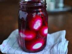 a glass jar filled with red liquid sitting on top of a wooden table next to a white towel