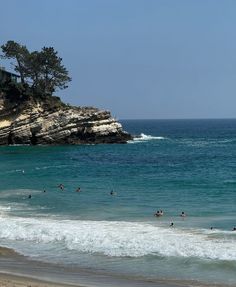 people are swimming in the ocean near an island with trees on top and cliffs above