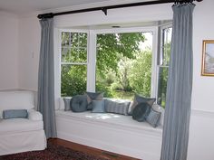 a window seat with pillows on it in front of a large window overlooking the trees