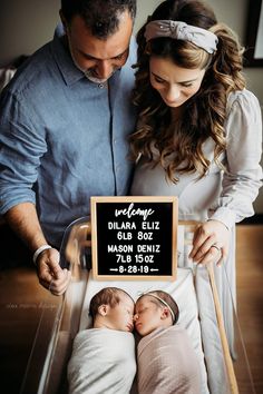 a man and woman standing next to a baby in a crib with a sign on it