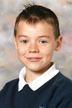 a young boy wearing a blue sweater and white collared shirt smiling at the camera