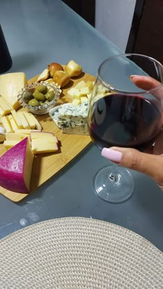 a person holding a glass of wine next to cheese and crackers