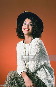 a woman sitting on top of a chair wearing a black hat and white cardigan