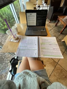 a laptop computer sitting on top of a wooden table next to a notebook and cup