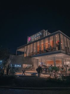 the exterior of a modern building at night with lights on and people walking around it