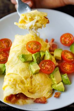 an omelet with tomatoes and avocado is being eaten on a plate