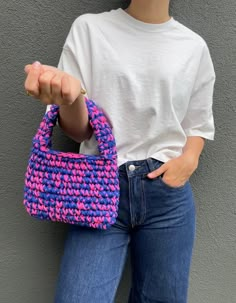 a woman is holding a pink and blue handbag in front of her back pocket