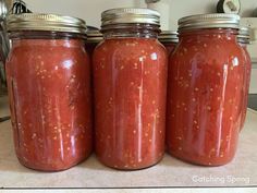 three jars filled with red sauce sitting on top of a counter