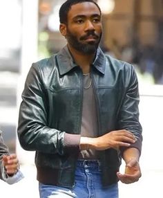 a man wearing a black leather jacket and jeans is walking down the street with his hands in his pockets