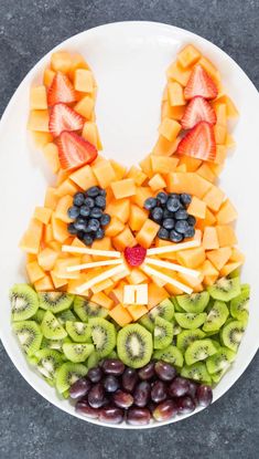 a white plate topped with sliced fruit and an animal made out of kiwis