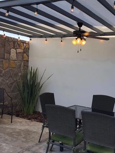 an outdoor dining table and chairs under a pergolated roof with lights hanging from the ceiling