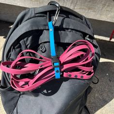 a black backpack with pink and blue straps on it's front pocket, next to a bench