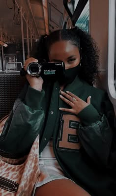 a woman wearing a green jacket and holding a camera in her hand while sitting on a train