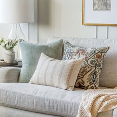 a white couch with several pillows on it and a lamp in the corner next to it