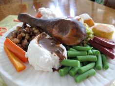 a white plate topped with meat, beans and veggies