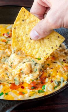 a hand dipping a tortilla chip into a skillet filled with chicken and cheese