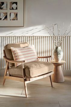 a chair and vase with flowers in it on a wooden floor next to a radiator