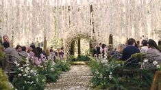 people are sitting in chairs at the end of an aisle with flowers hanging from it