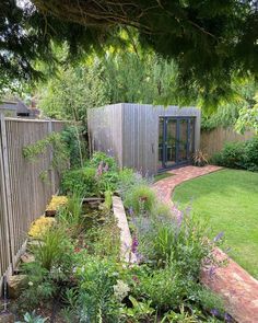 a garden with lots of plants and flowers in the grass next to a wooden fence