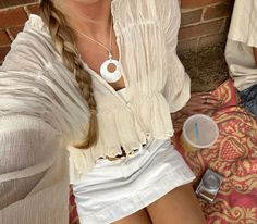 a woman sitting next to a brick wall with a cell phone and cup in her hand