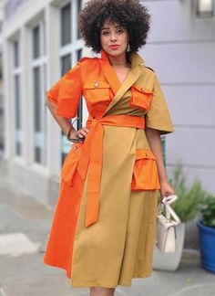 a woman in an orange and yellow dress is standing on the sidewalk with her hands on her hips