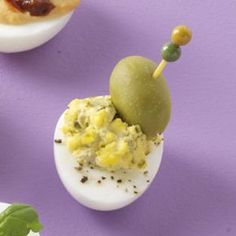 three deviled eggs with pickles and olives on them sitting on a purple surface