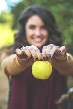 a woman holding an apple in front of her face with both hands and smiling at the camera