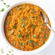 a white bowl filled with carrot curry and garnished with cilantro leaves