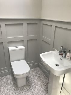 a white toilet sitting next to a sink in a bathroom under a window with gray paneling