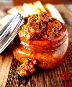 a jar filled with sauce next to french fries on top of a wooden table,