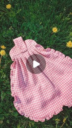 a pink and white checkered dress laying on the grass with dandelions in the background