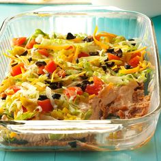 a glass casserole dish filled with meat, vegetables and cheese on a blue table