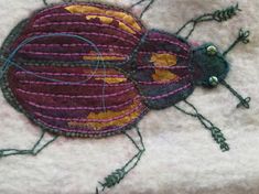 an embroidered bug sitting on top of a white cloth covered tablecloth with green and purple thread