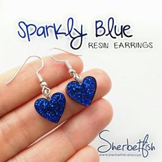 a pair of blue heart shaped earrings are shown in front of a white background with the words sparkly blue resin earrings