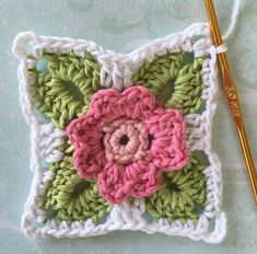 a crocheted square with pink and green flowers on it next to a knitting needle