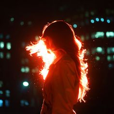 a woman standing in front of a city at night with her hair blowing in the wind