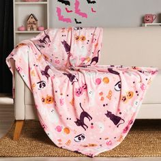 a pink blanket with cats and bats on it is draped over a couch in a living room