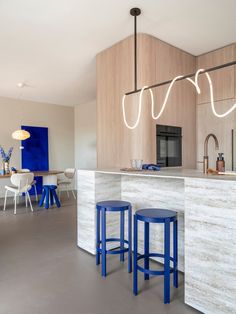 a kitchen with two blue stools next to a counter and an island in the middle